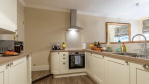 A kitchen with white cabinets, a built-in oven, a stainless steel range hood, and a wooden countertop. - 71 Micklegate - Apartment 2 (York)