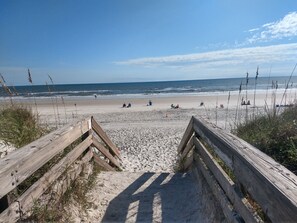 A sandy beach with wooden walkways leading to the water, and people sitting and walking along the shore.