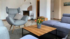 Un salon moderne avec un fauteuil gris, un canapé bleu et une table basse en bois. On y trouve une cheminée avec une arche en briques, un présentoir en métal et un vase rempli de fleurs.