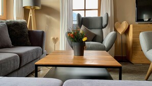 Un salon moderne avec un canapé gris, une table basse en bois, un fauteuil gris et un téléviseur fixé au mur.