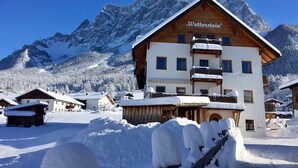 Un bâtiment en bois portant l’inscription « Wetterstein » sur sa façade, entouré de montagnes enneigées.
