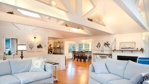 A spacious living area with a high ceiling, wooden flooring, and light-colored furniture.