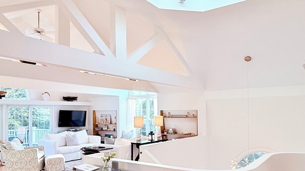 A spacious living area with a high ceiling, a curved white partition, and a flat-screen TV.