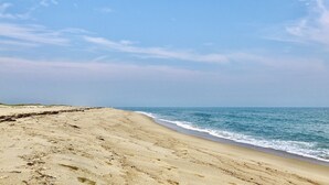 A wide sandy beach with gentle waves, clear skies, and a distant horizon.
