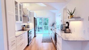 A modern kitchen with white cabinetry, a built-in oven, a refrigerator, and a coffee machine.
