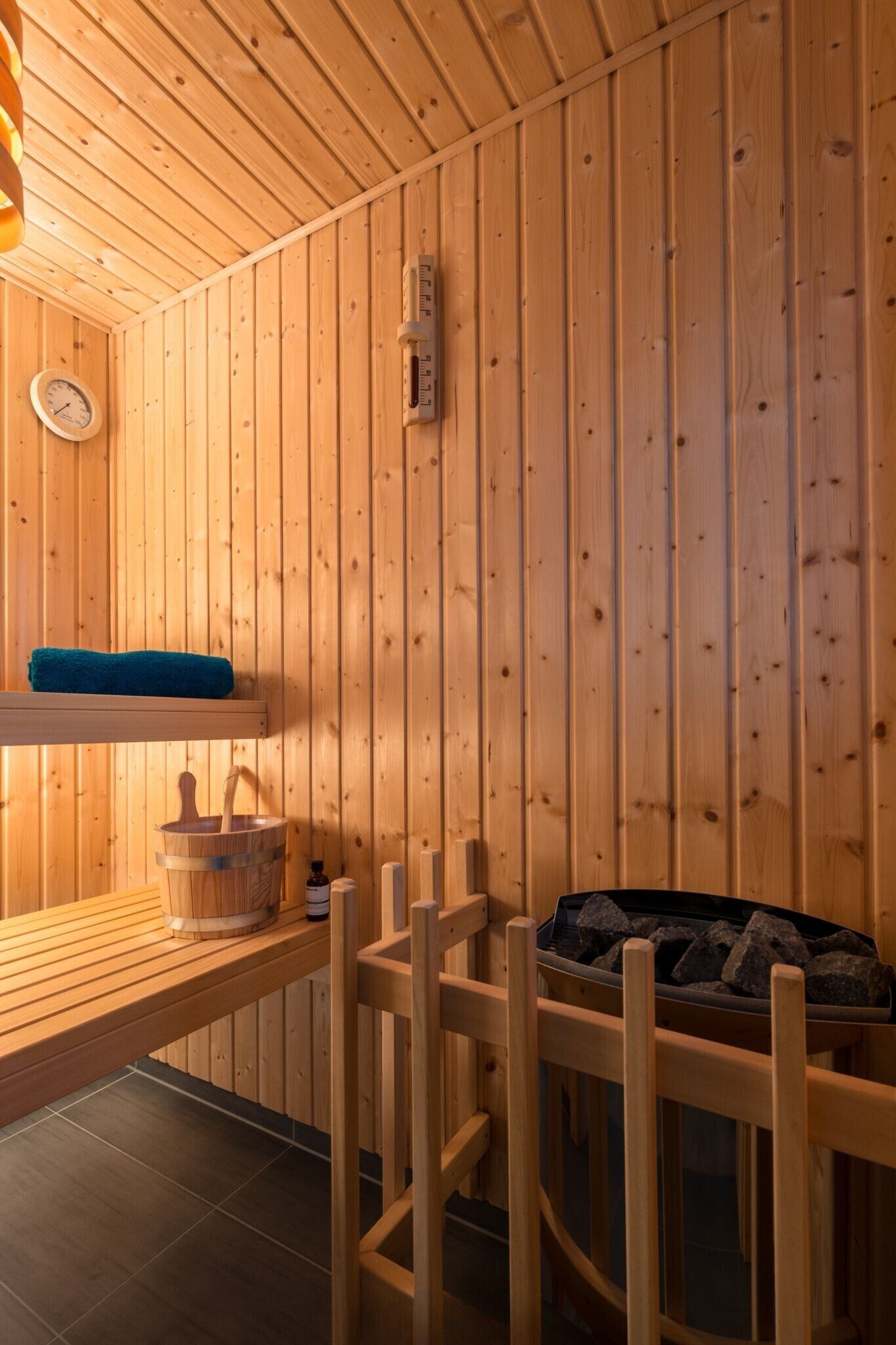 A wooden sauna room with a wooden bench, a bucket, and a heater.