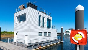 A white houseboat docked at a pier with a clear blue sky. - Water house "The Nordic House" at Ostseeresort Olpenitz - sun deck & sea view (Olpenitz)