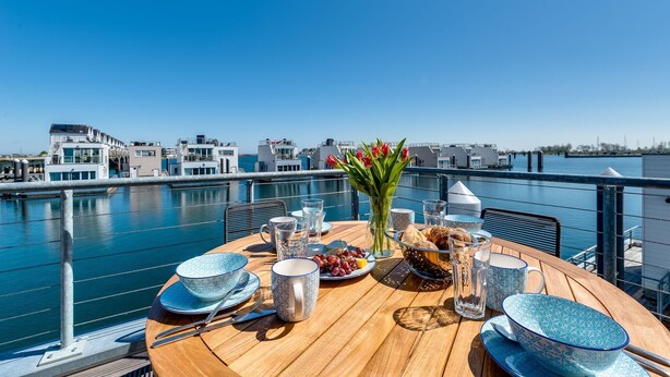 A table set for breakfast with a view of the water and buildings in the background. - Water house "The Nordic House" at Ostseeresort Olpenitz - sun deck & sea view (Olpenitz)