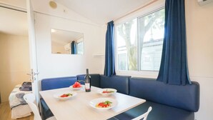A dining area with a table, chairs, and a bench. There are plates with food and a bottle on the table. - Happy Camp in Camping Village Paestum (Eboli)