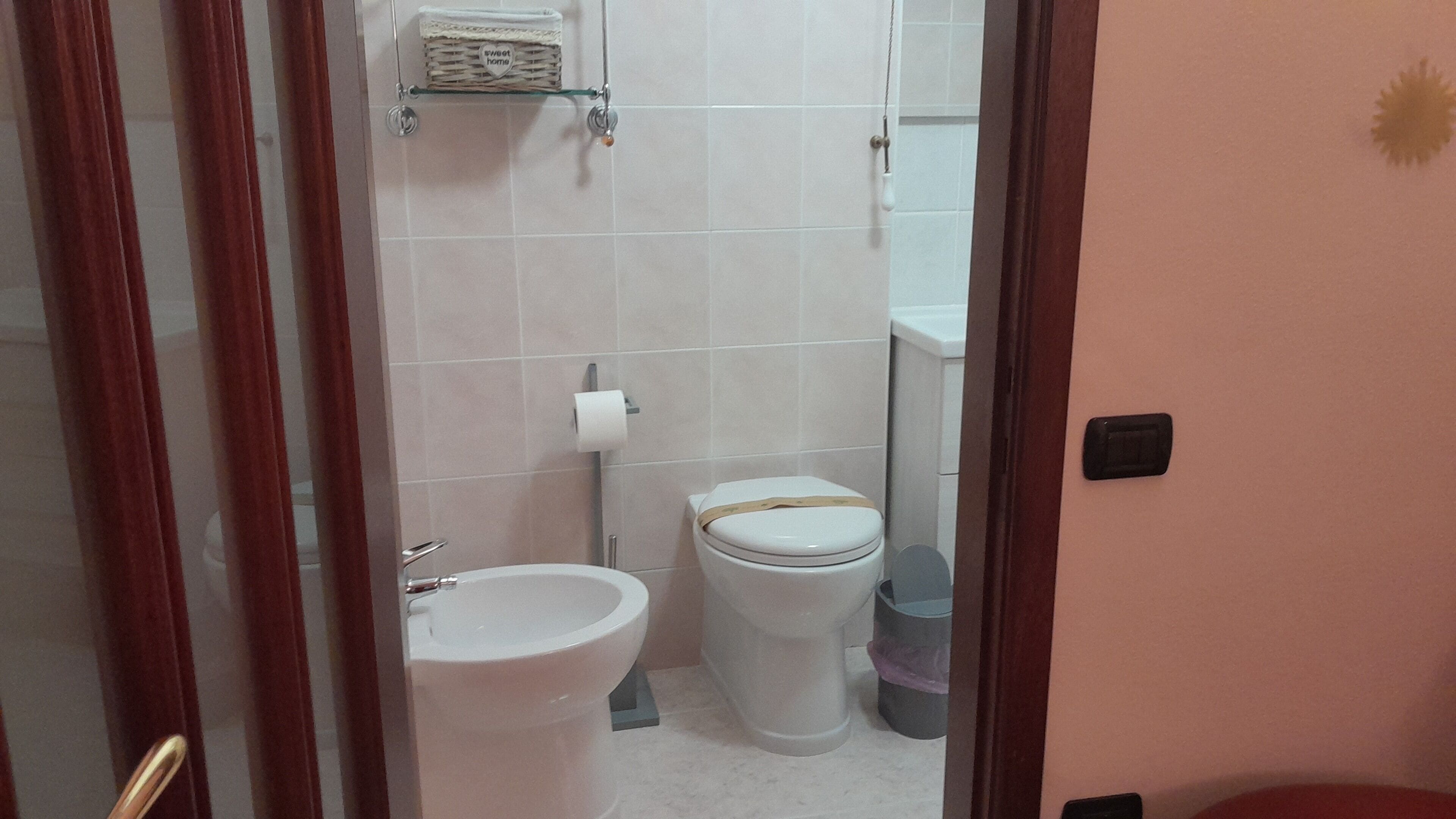 Une salle de bain équipée de toilettes, d’un bidet et d’une petite étagère sur laquelle se trouve un panier.