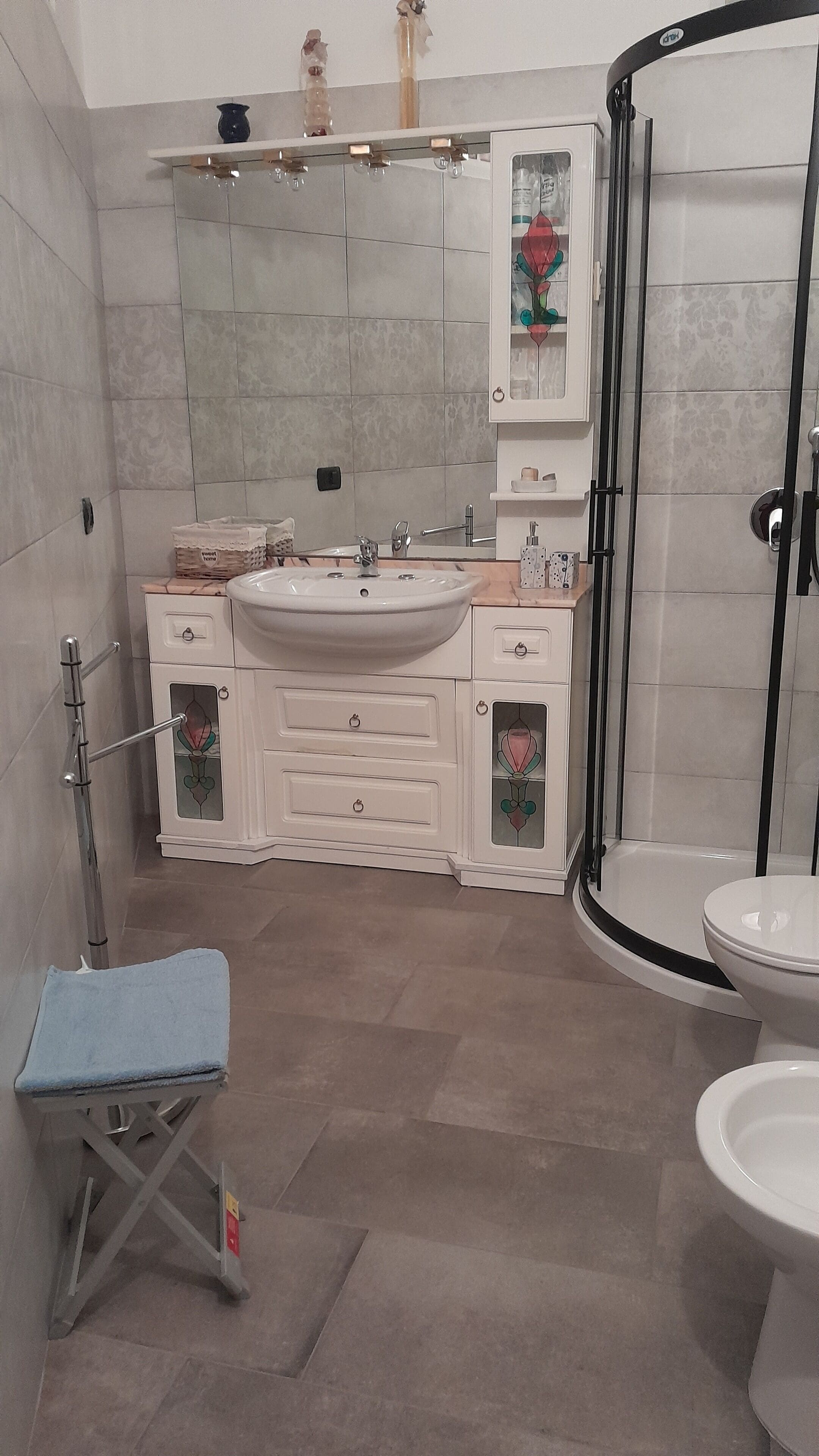 Un baño con tocador blanco, cabina de ducha de vidrio y banco azul.