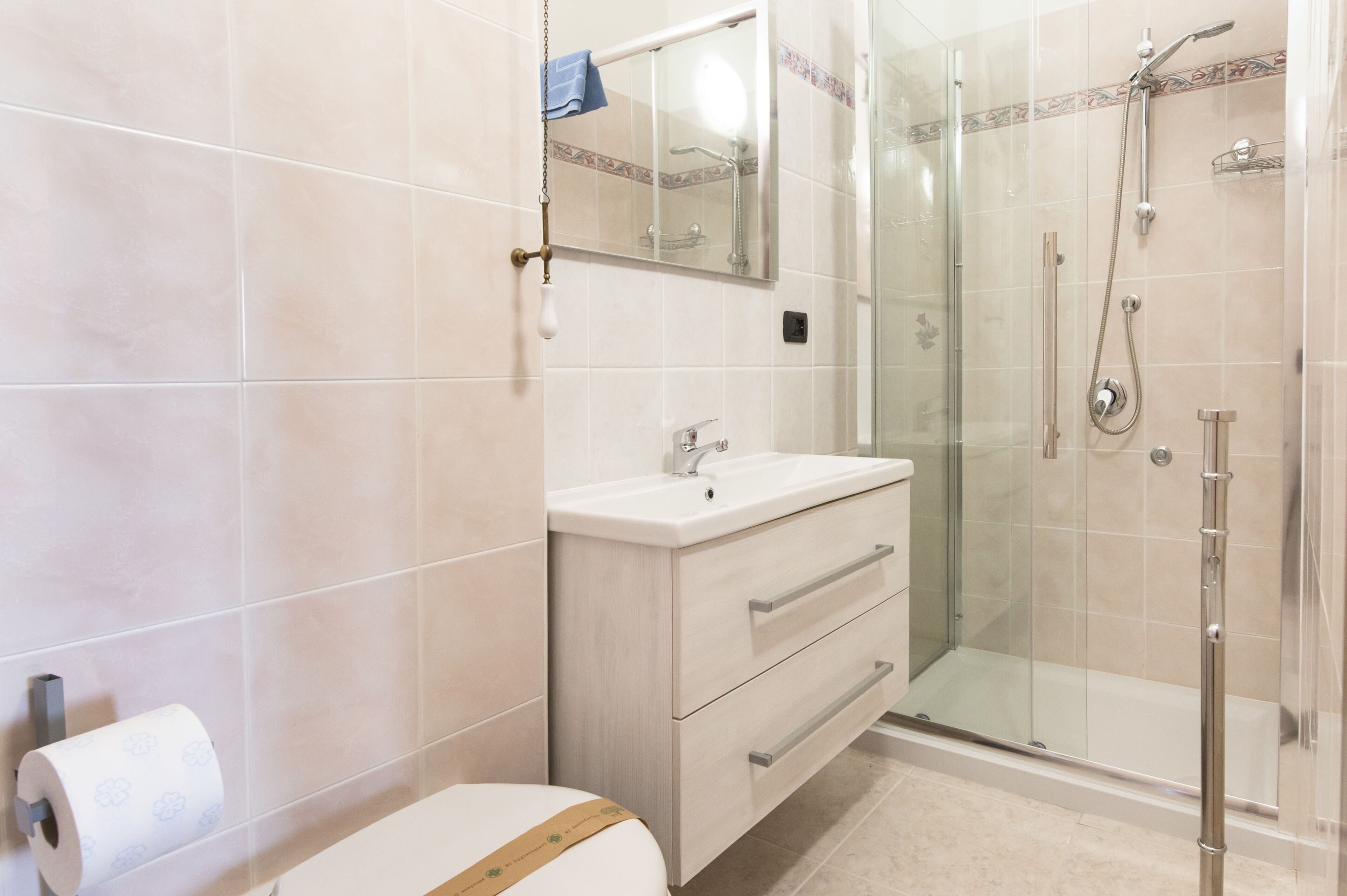 Un baño con inodoro, lavamanos con espejo y zona de ducha con mampara de vidrio.