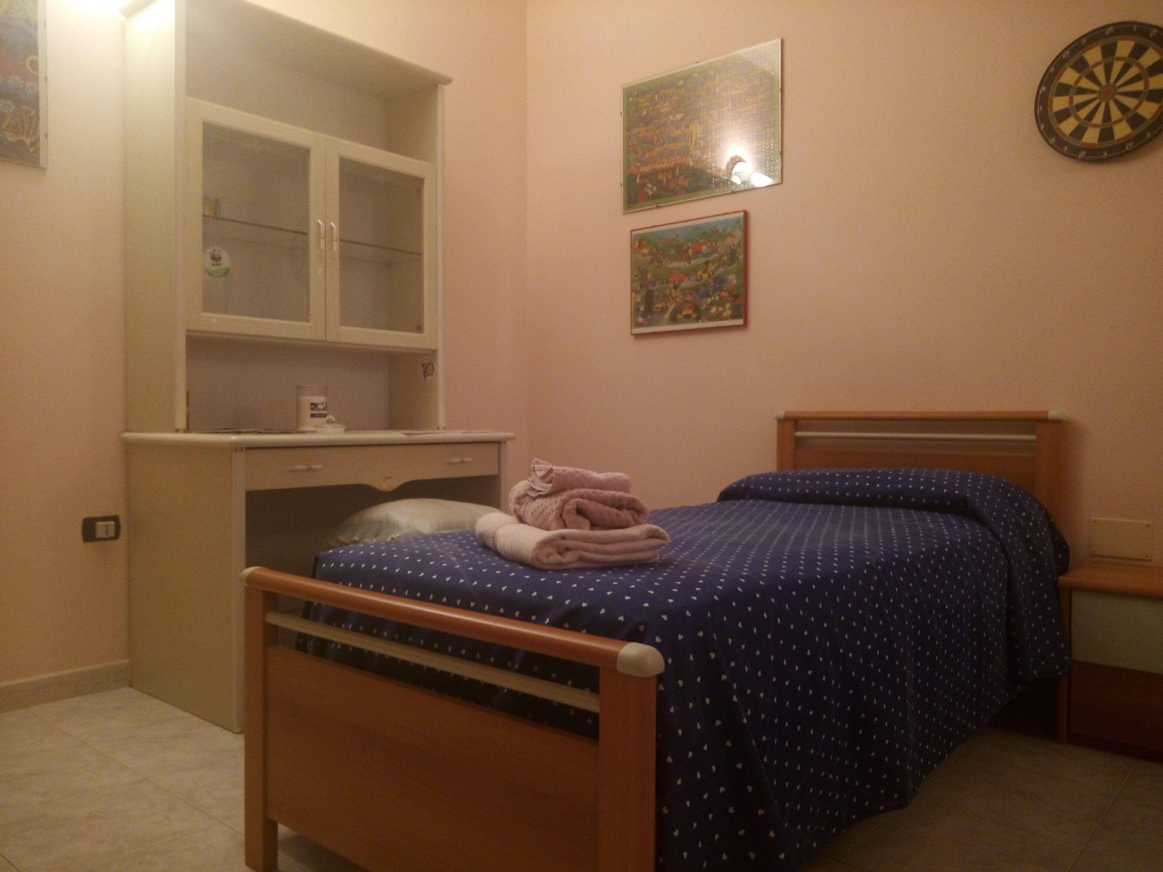 Un dormitorio con cama, cabecera de madera, mesita de noche, espejo y dardo en la pared.