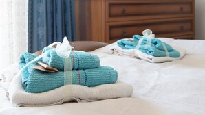 Een net opgemaakt bed met opgevouwen handdoeken en een televisie op een houten dressoir op de achtergrond.