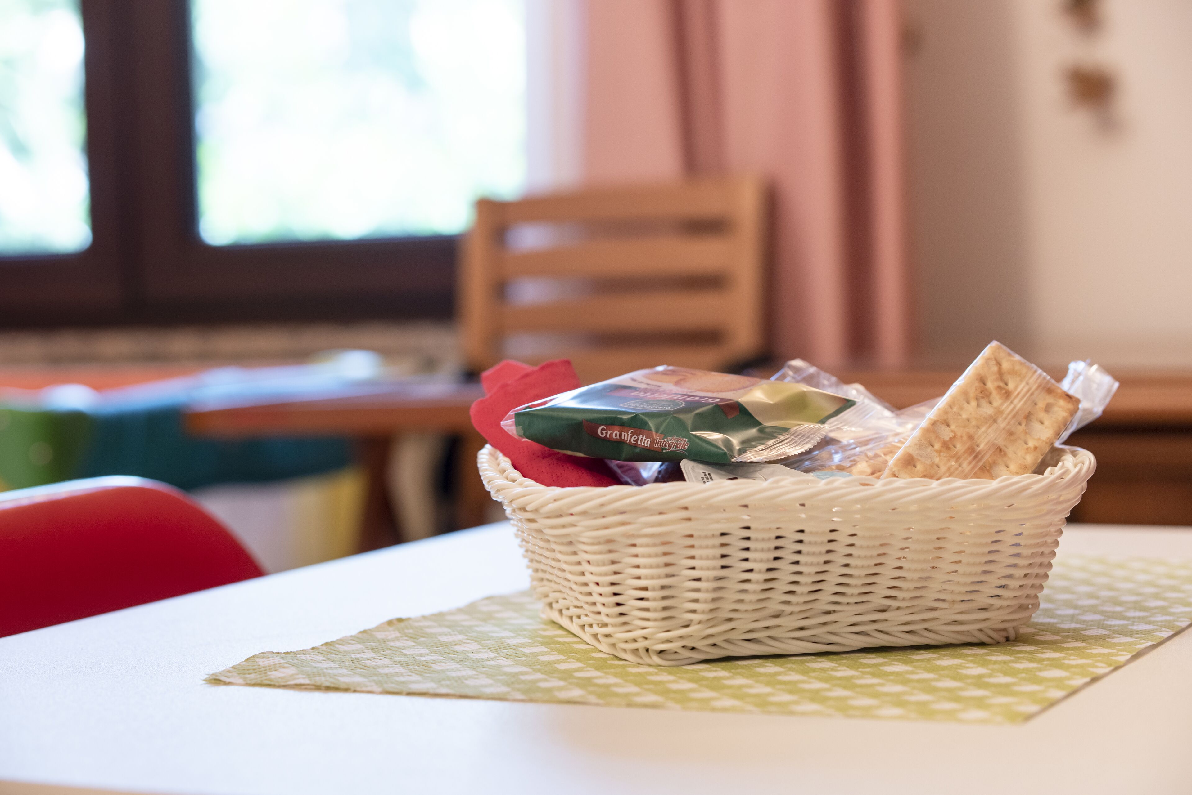 A wicker basket on a table with a green placemat, containing a red cloth, a green package, and a brown package.