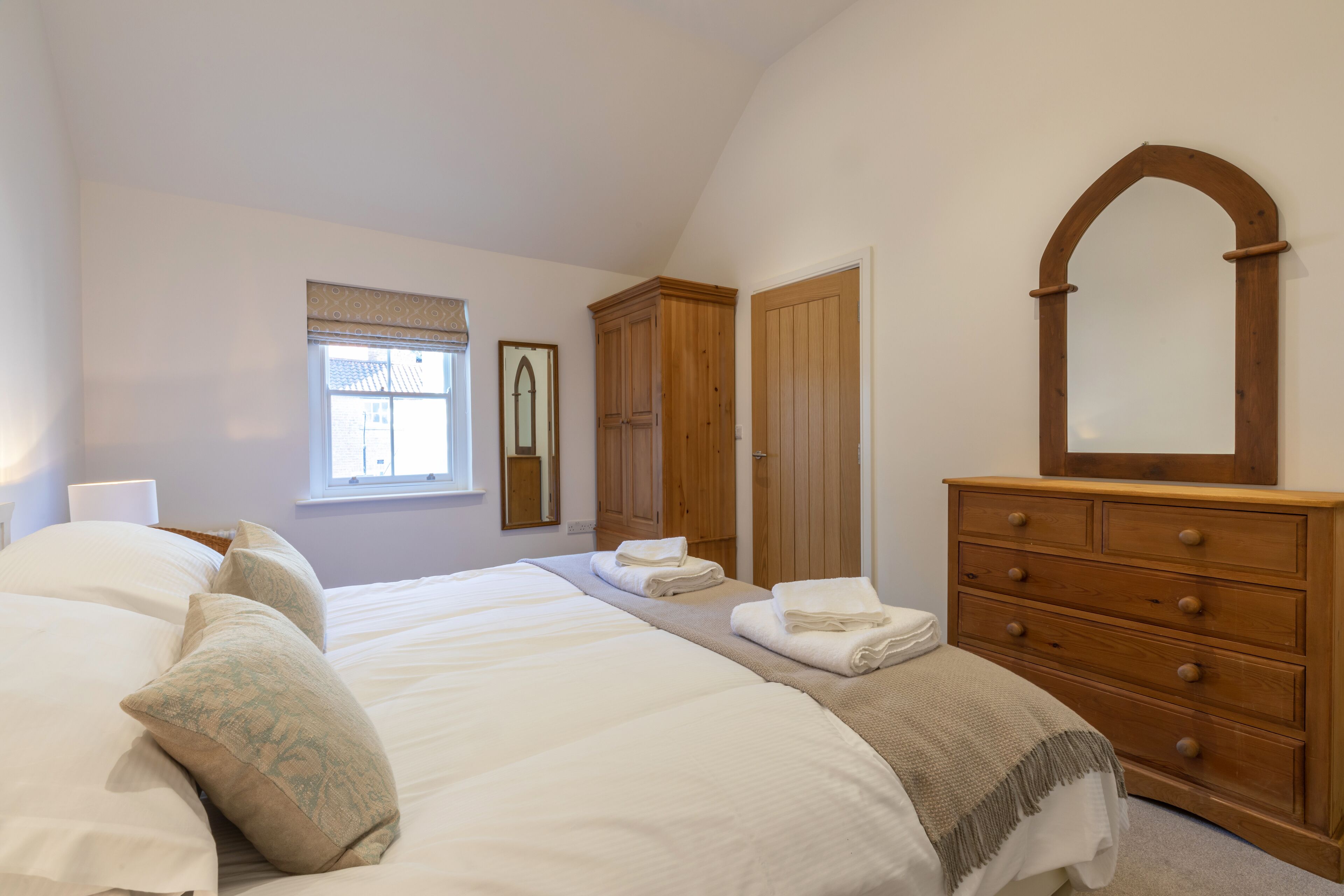 Une chambre avec deux lits, une armoire en bois et un miroir.