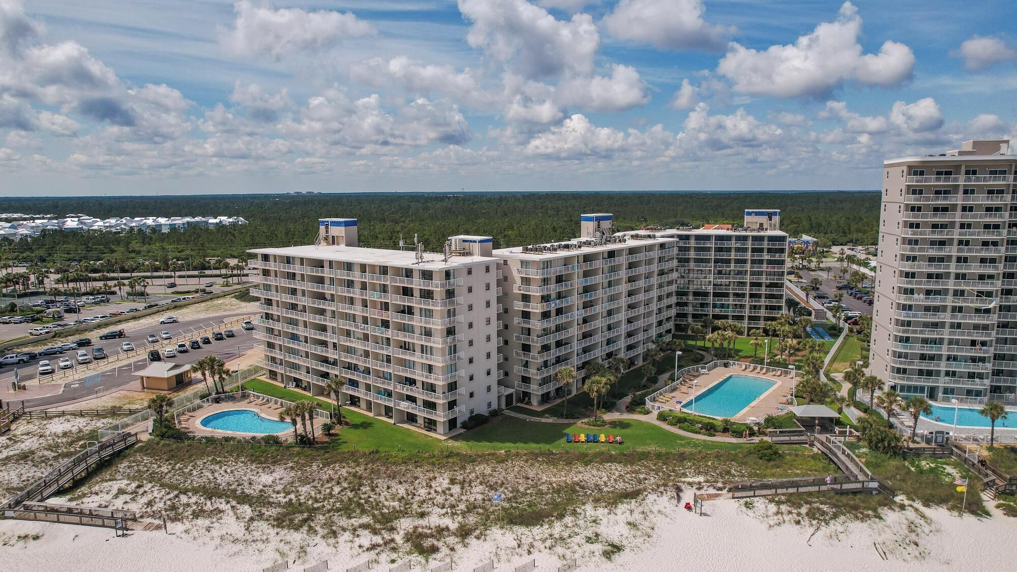 Ein mehrgeschossiges Hotel mit Poolbereich, umgeben von einem Strand und einem Parkplatz.