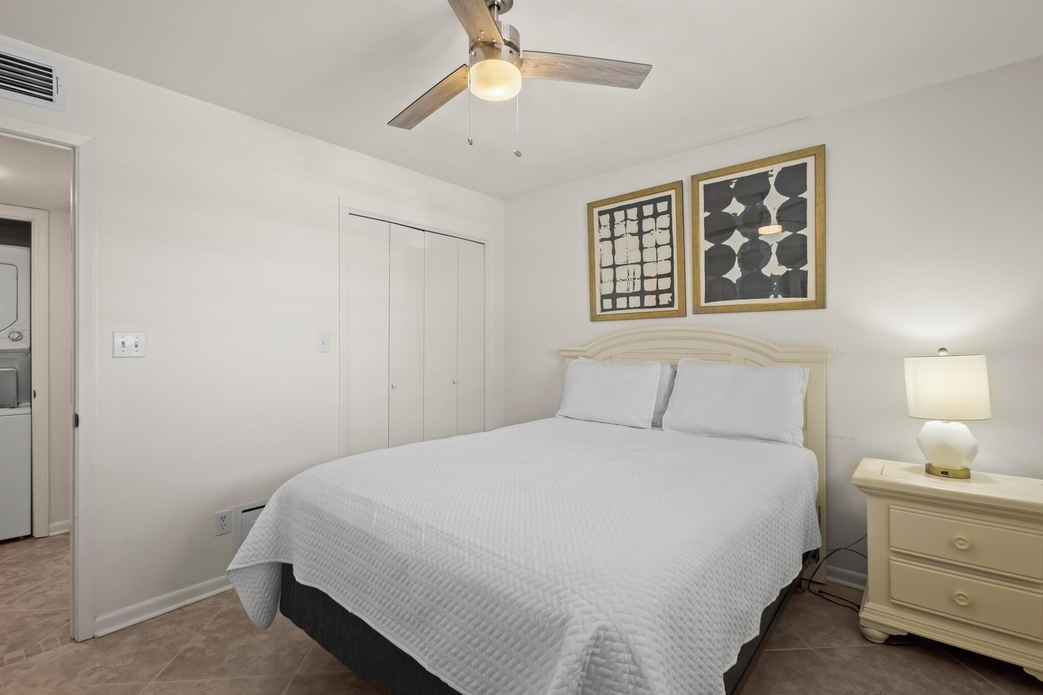 A bedroom with a bed, a nightstand, a ceiling fan, and two framed pictures on the wall.
