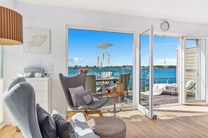 Una sala moderna con vista al mar, un comedor con una mesa dispuesta para dos personas y un balcón con vistas al agua.