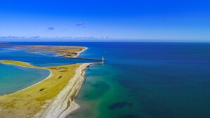 An aerial view of a coastal area with a lighthouse, sandy beaches, and clear blue waters.