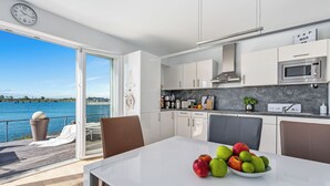A modern kitchen with a view of the water, a dining area with a table and chairs, and a clock on the wall.