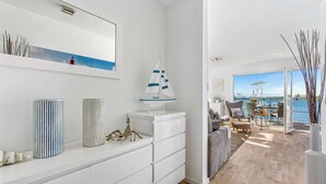 A modern living room with a white console table, a decorative sailboat, and a view of the water through large windows.