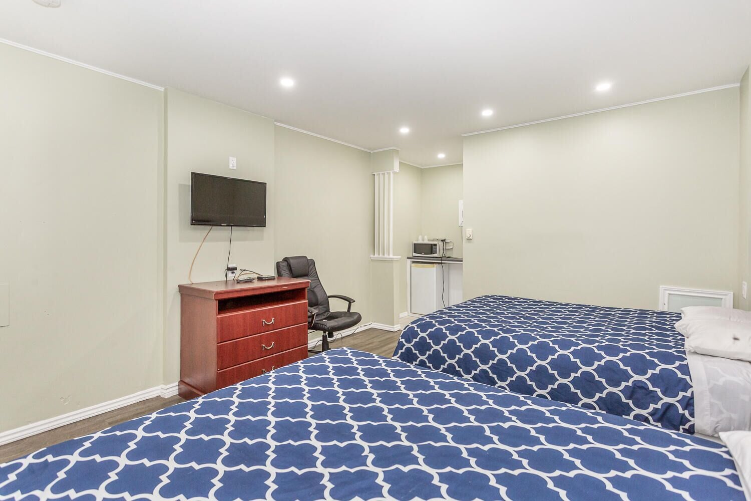 Un dormitorio con dos camas, un escritorio, una silla, un televisor y una kitchenette pequeña.