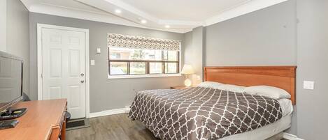 A bedroom with a bed, a desk, a chair, a window with a view, and a door.