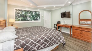 A bedroom with a bed, a desk, a chair, a TV, and a dresser. - Haven Inn (Hamilton)