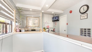 A reception area with a reception desk, a clock, a television, and a sign indicating check-out time. - Haven Inn (Hamilton)