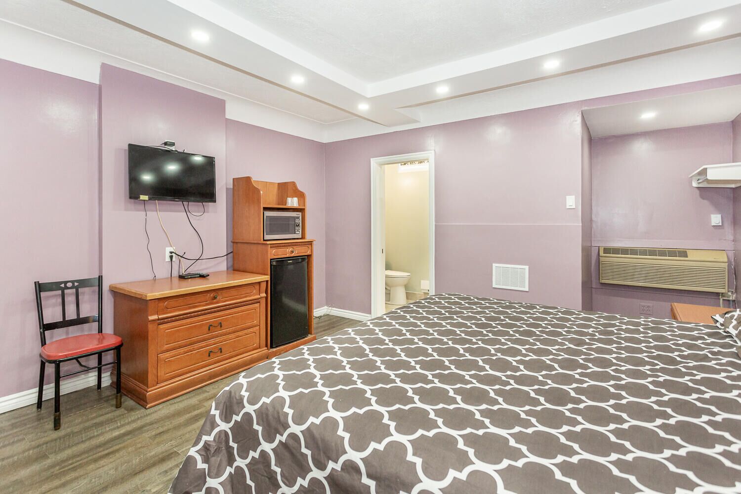 A bedroom with a bed, a dresser, a TV, and a microwave.