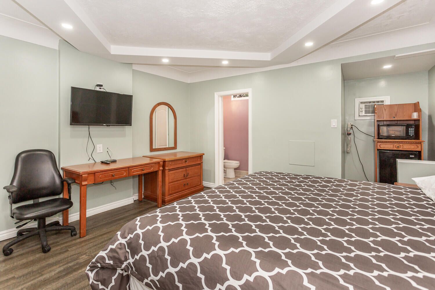 Une chambre à coucher comprenant un lit, un bureau, une chaise, une télévision, un miroir, un four à micro-ondes et des toilettes.