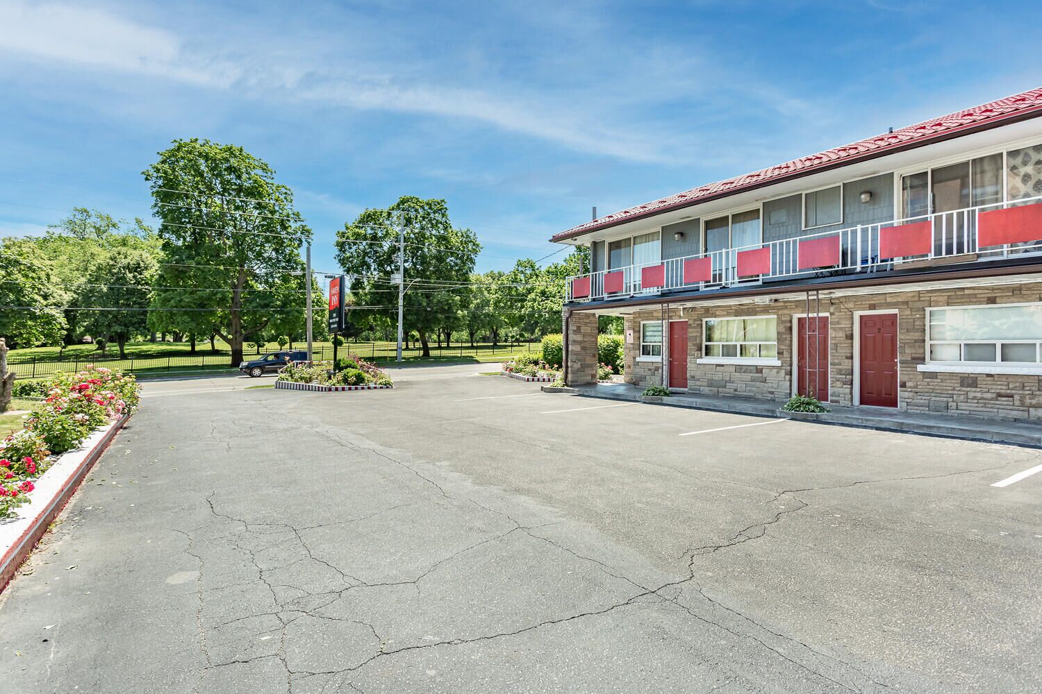 Un motel composé d’un bâtiment à deux étages, d’un parking et d’un espace paysager agrémenté d’arbres et de fleurs.