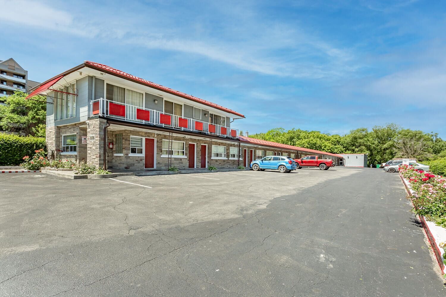 A motel with a red roof, multiple rooms, and a parking lot.