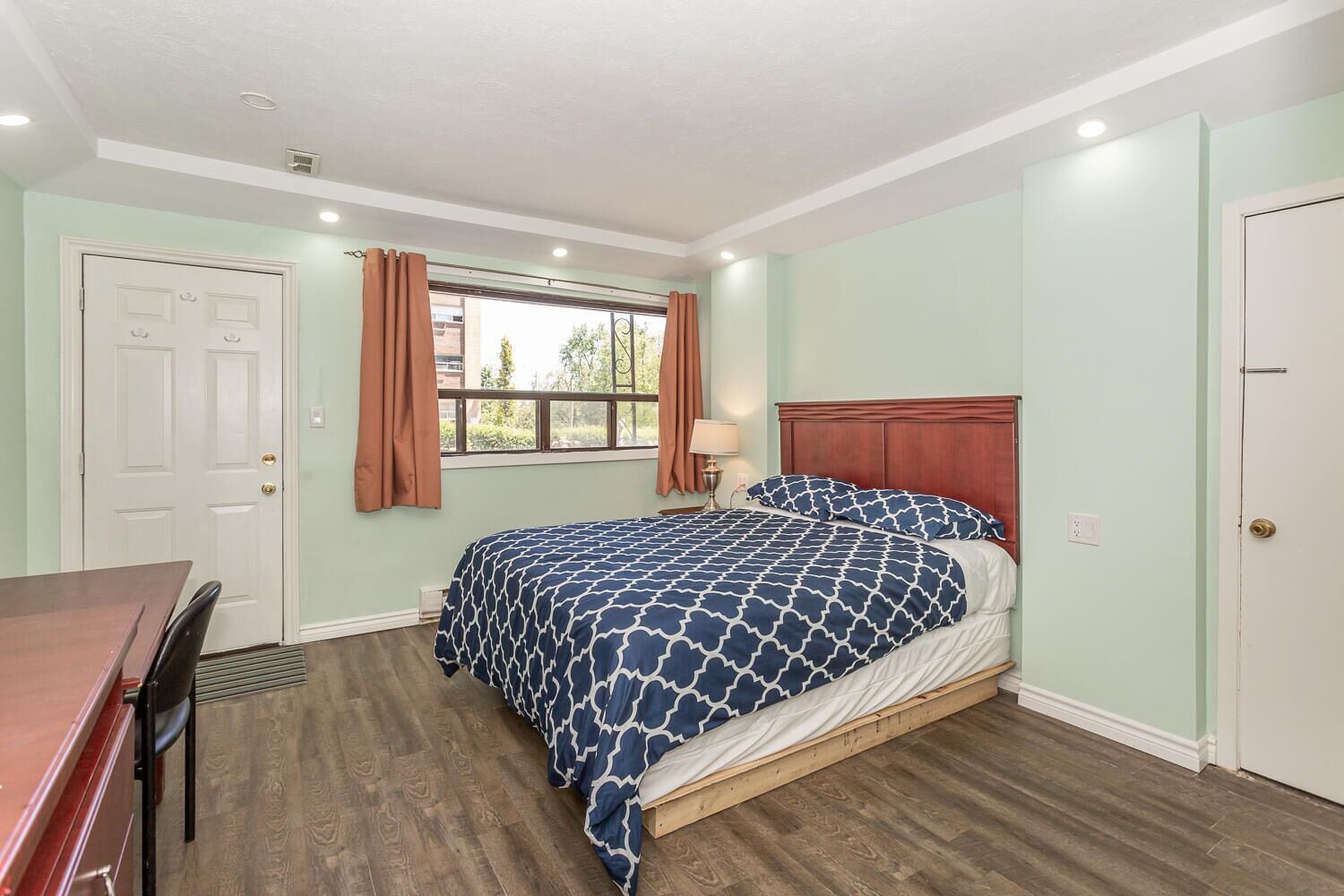 A bedroom with a bed, a desk, and a window with curtains.