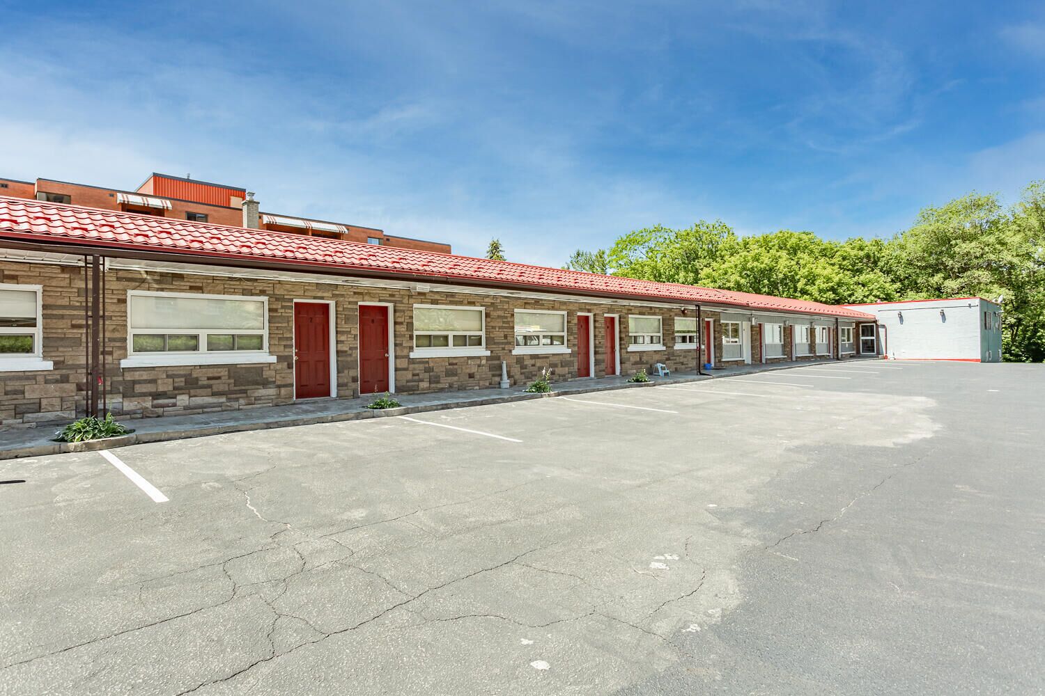 A row of motel rooms with a red-tiled roof, a parking lot, and a clear sky.