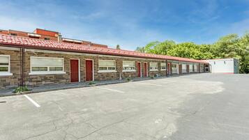 A row of motel rooms with a red-tiled roof, a parking lot, and a clear sky.