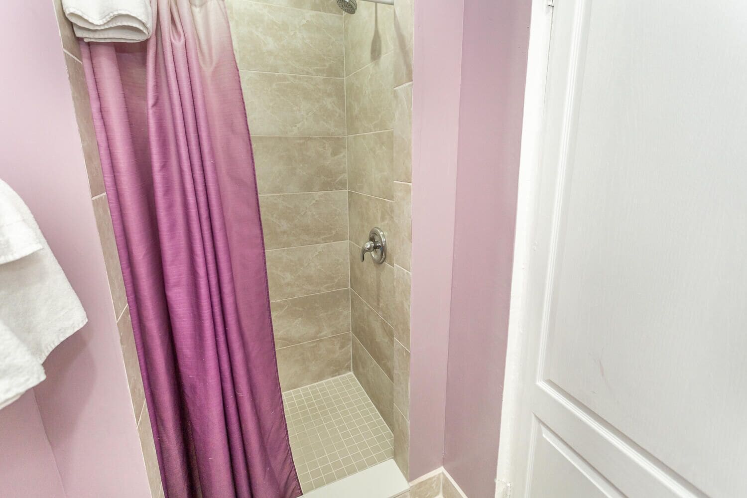 A bathroom with a shower, tiled walls, and a white door.