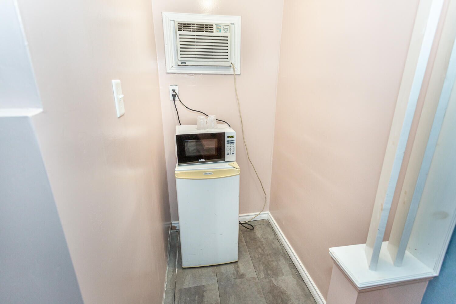 Une petite buanderie comprenant un lave-linge et un sèche-linge, une petite fenêtre avec des stores et un climatiseur fixé au mur.