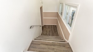 A narrow stairway with wooden steps and white walls, leading to a landing with a window. - Haven Inn (Hamilton)