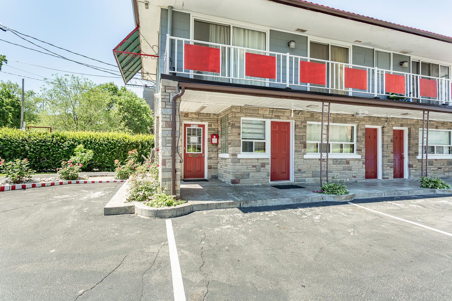 A motel with a two-story structure, a red door, and a balcony with red curtains.