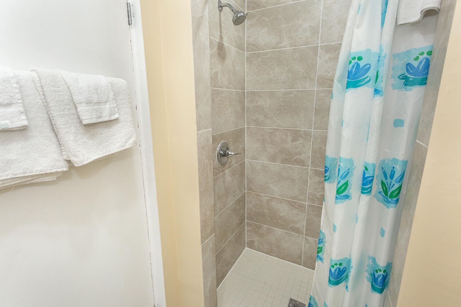 A bathroom with a shower, tiled walls, and a curtain with a blue and green pattern.
