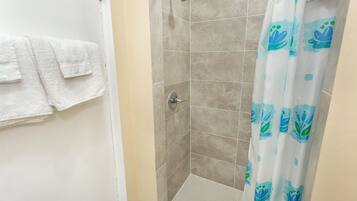 A bathroom with a shower, tiled walls, and a curtain with a blue and green pattern.