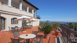 Una terraza con mobiliario exterior, plantas en macetas y vistas del paisaje.