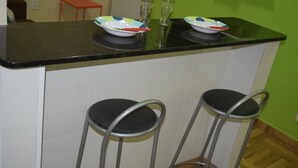 Een keuken met een zwart aanrecht, twee barkrukken en een groene wand.