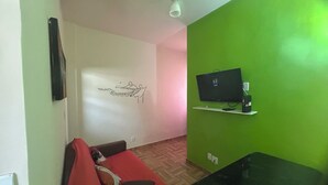 Een kamer met een rode bank, een televisie aan een groene muur en een witte plafondlamp.