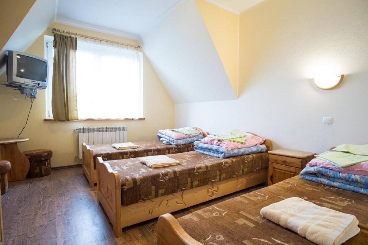 A small, cozy room with two wooden beds, a small table, a chair, a television, and a window with curtains.