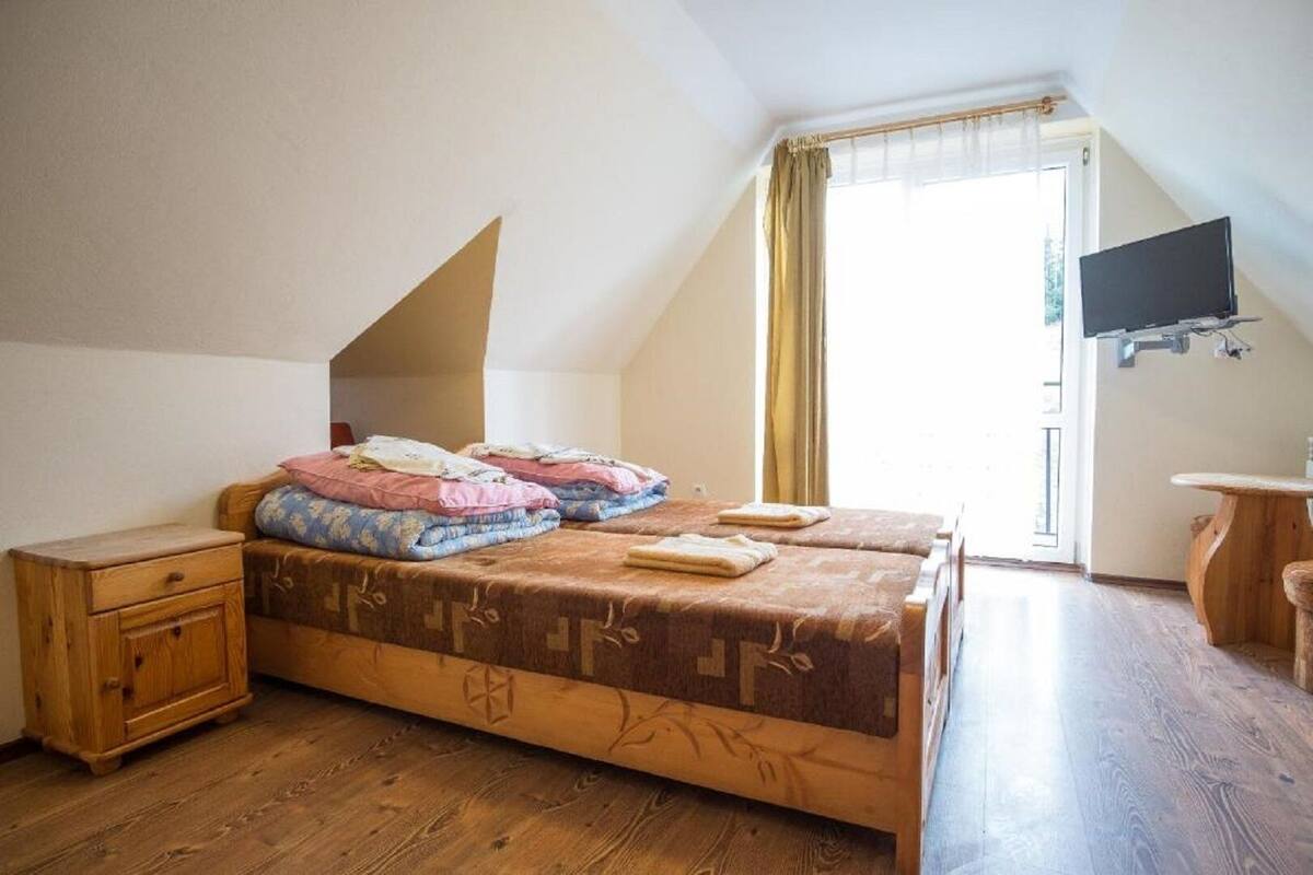 A bedroom with a large bed, a wooden nightstand, a small table, and a TV mounted on the wall.
