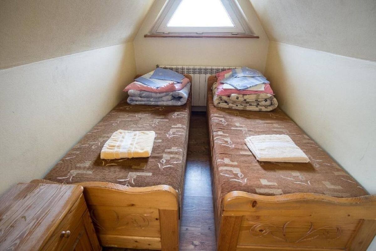 A small, narrow room with two wooden beds, a slanted ceiling, and a skylight.
