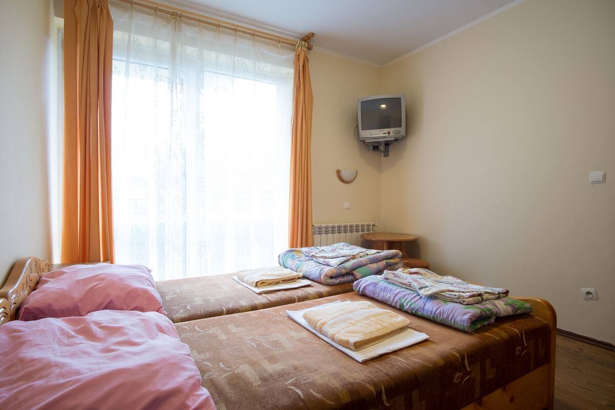 A hotel room with two beds, a television mounted on the wall, and a window with curtains.
